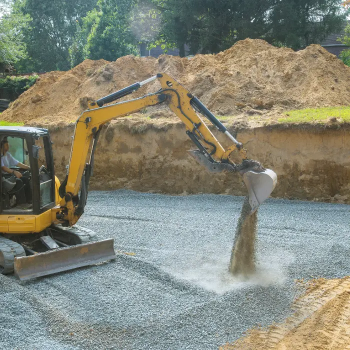 Mini-pelle mettant en place du gravier sur une plateforme de construction